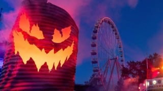 A glowing jack-o'-lantern and a lit Ferris wheel at a Six Flags Fright Fest at night