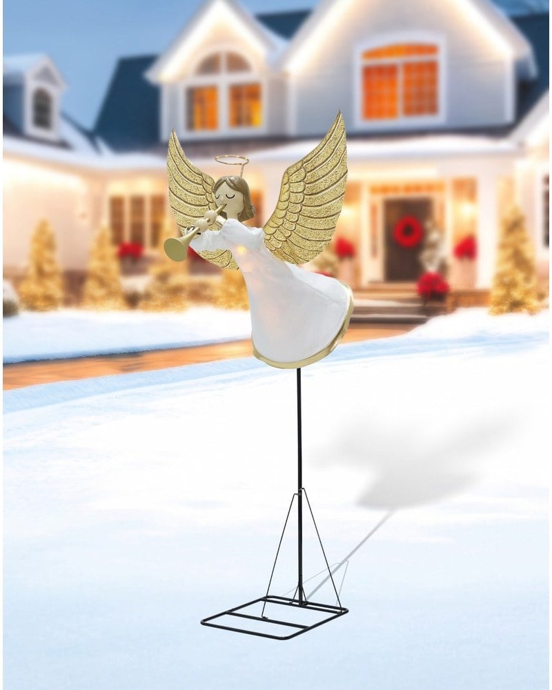 A tall angel prop with gold wings and a trumpet on a stand in a snowy yard