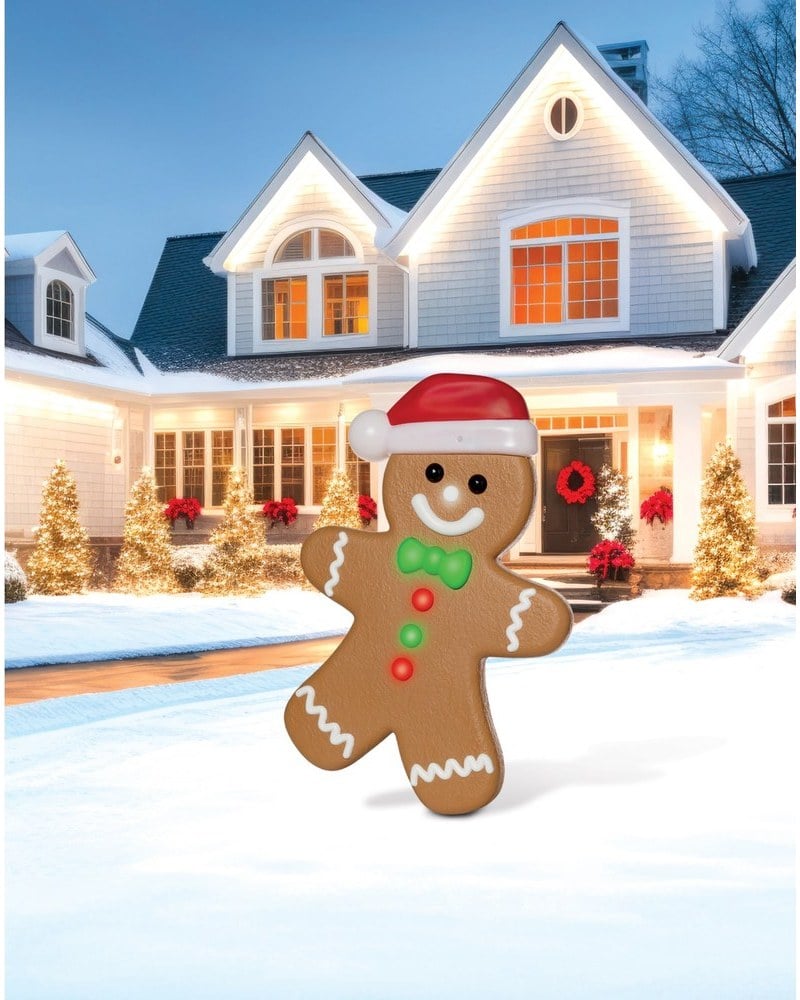 A gingerbread boy animatronic in a Santa hat on a snowy lawn