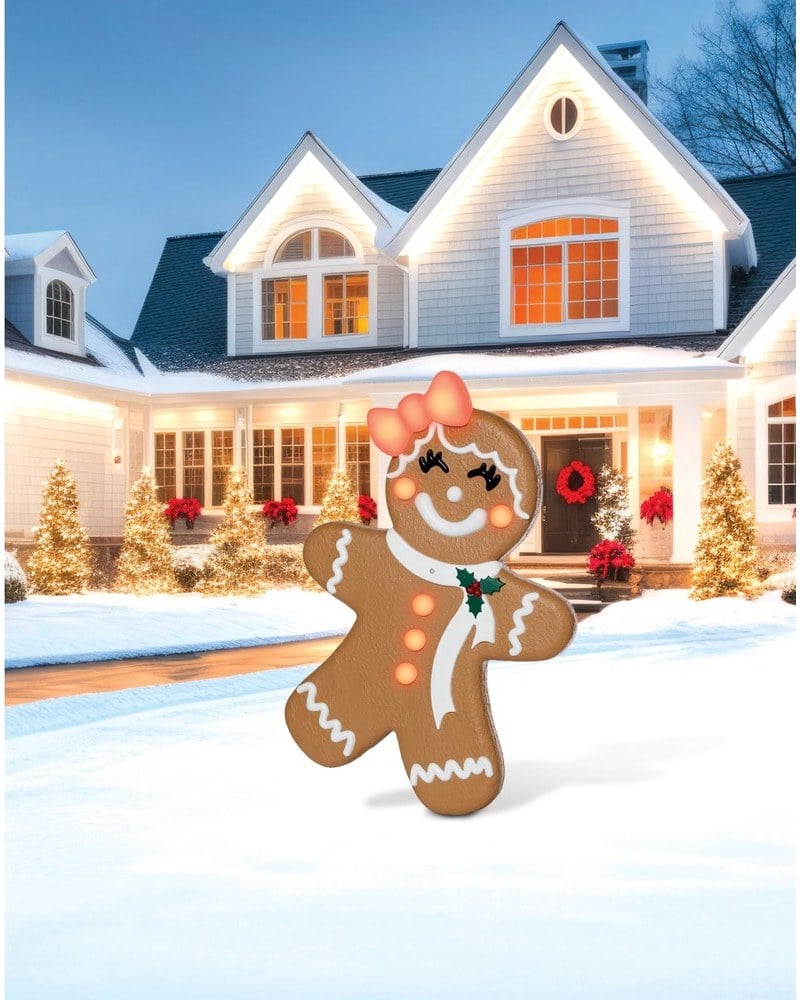 A gingerbread girl animatronic with a pink bow on a snowy lawn