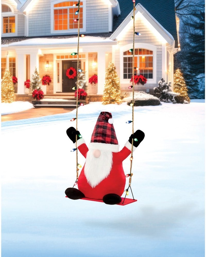 A gnome in a red plaid hat sitting on a swing hung with lights