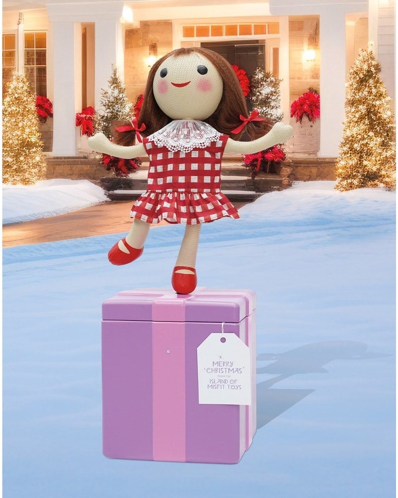 A Misfit Doll animatronic in a red gingham dress standing on a pink gift box
