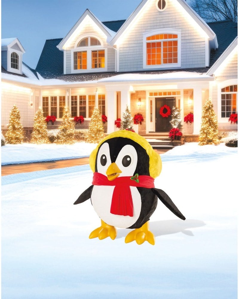 A penguin animatronic in yellow earmuffs and a red scarf on a snowy lawn