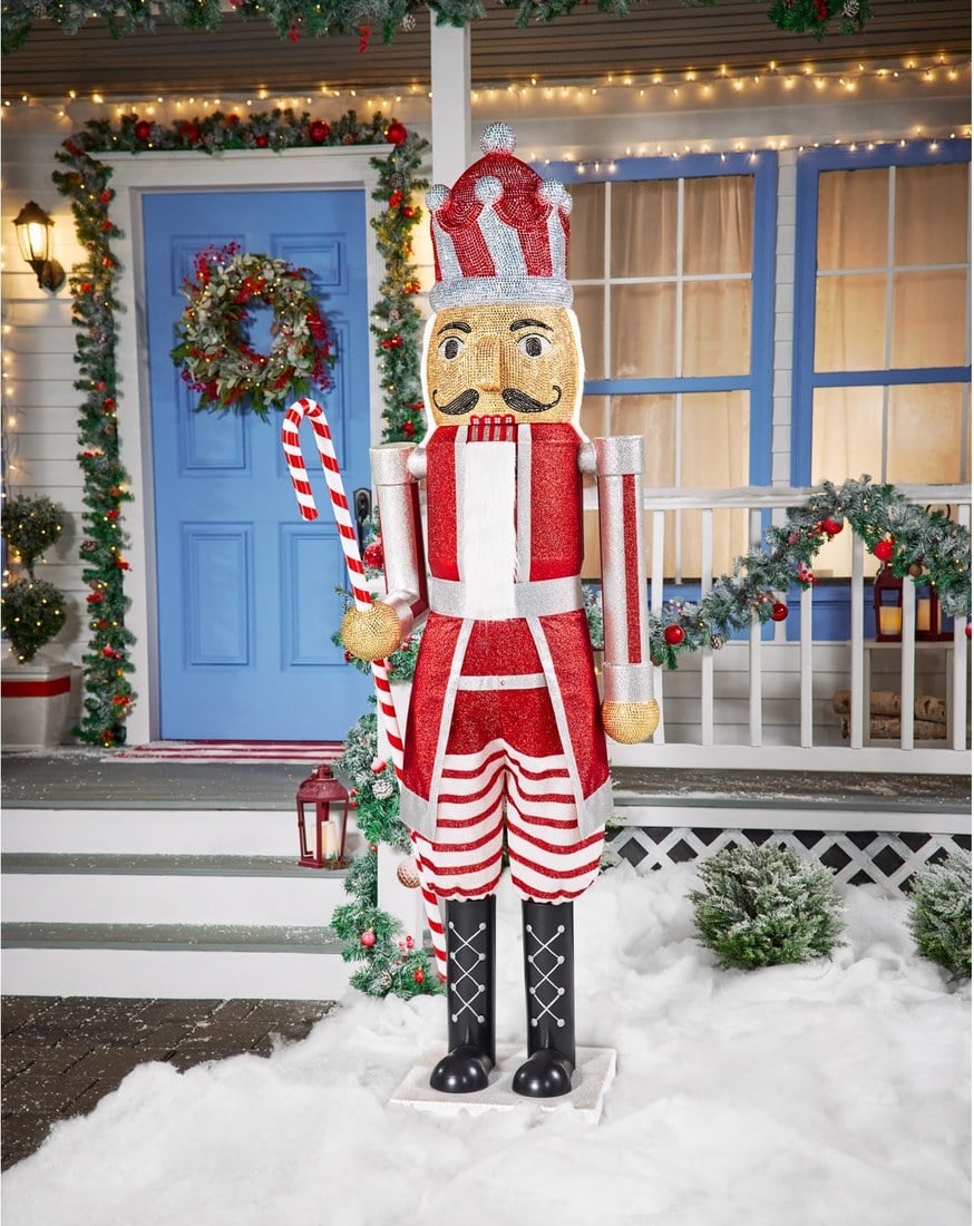A 7-foot red-and-white Candy Cane nutcracker animatronic holding a candy cane beside a front door