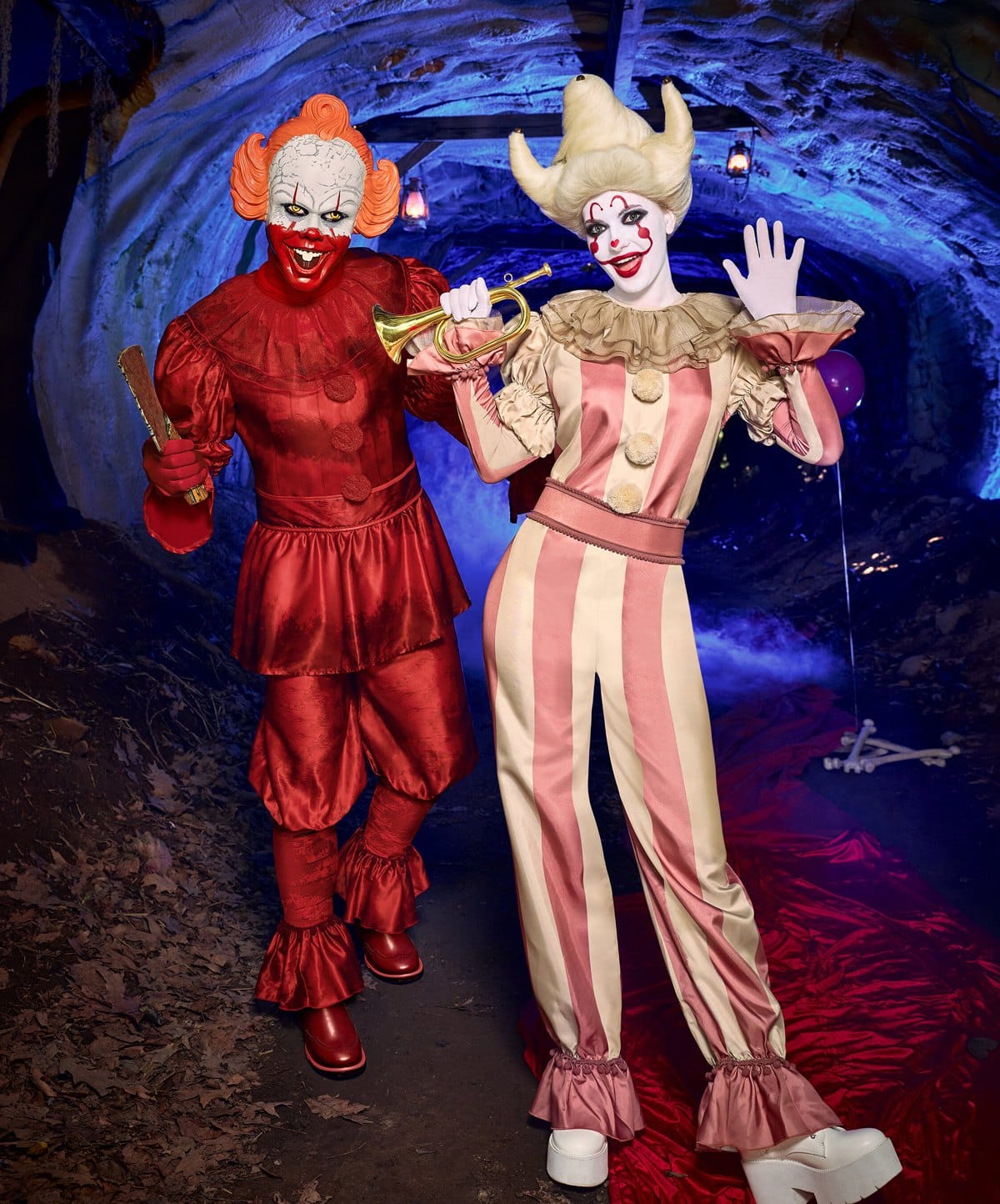 Two adults in clown costumes, one in red with orange hair and one in pink and cream stripes holding a horn