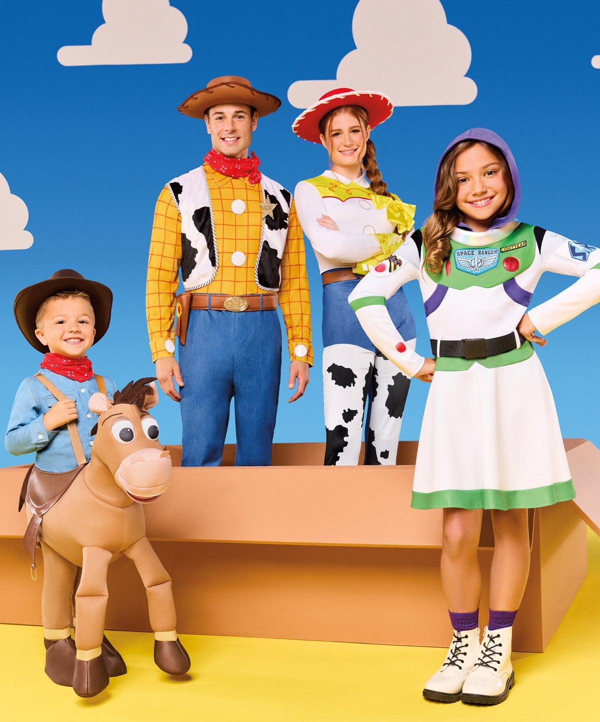 An adult in a Woody costume, an adult in a Jessie costume, a girl in a Buzz Lightyear dress costume, and a toddler in a Bullseye ride-along costume