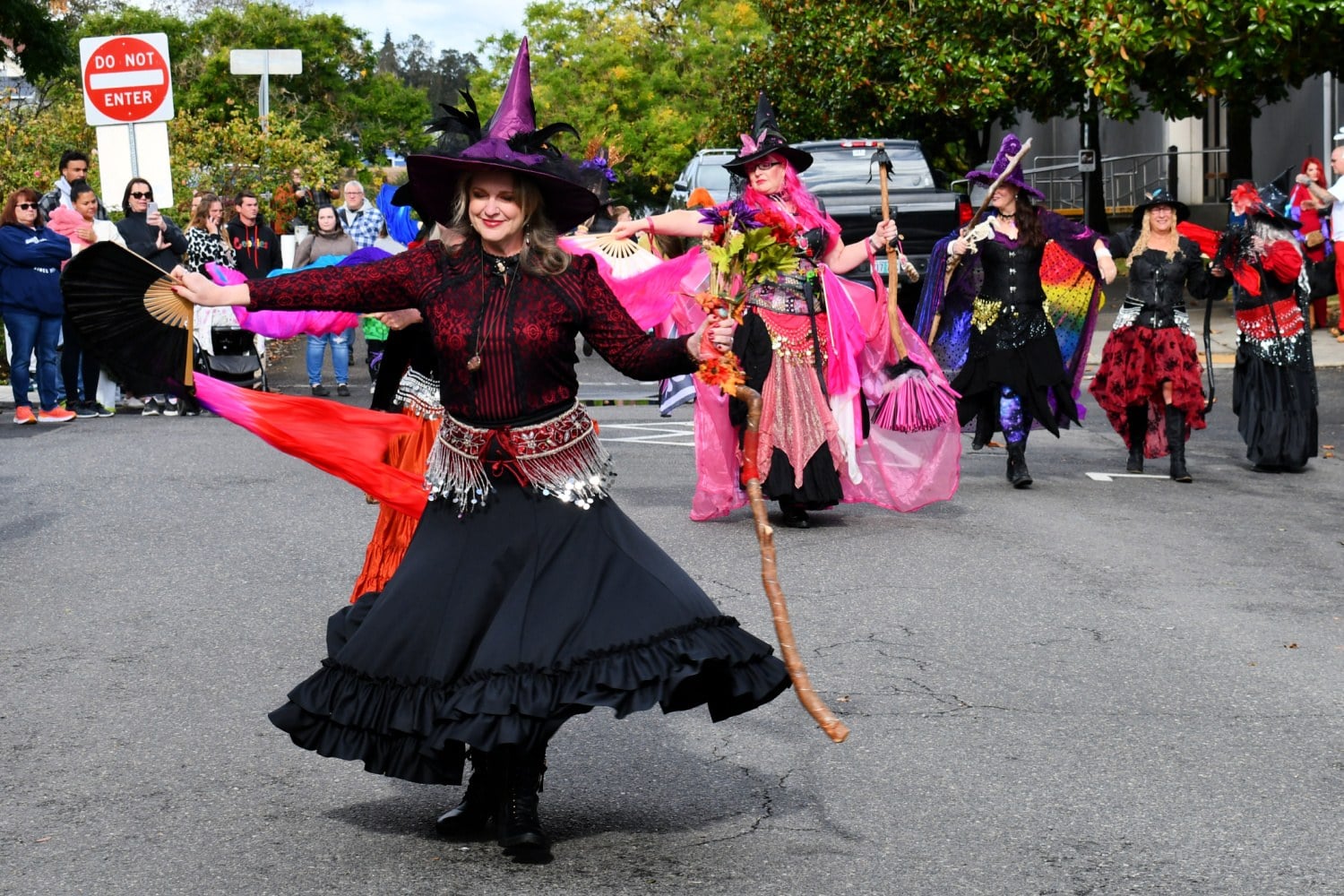 Costumed witches in black and pink dance down a street in St. Helens as a crowd watches