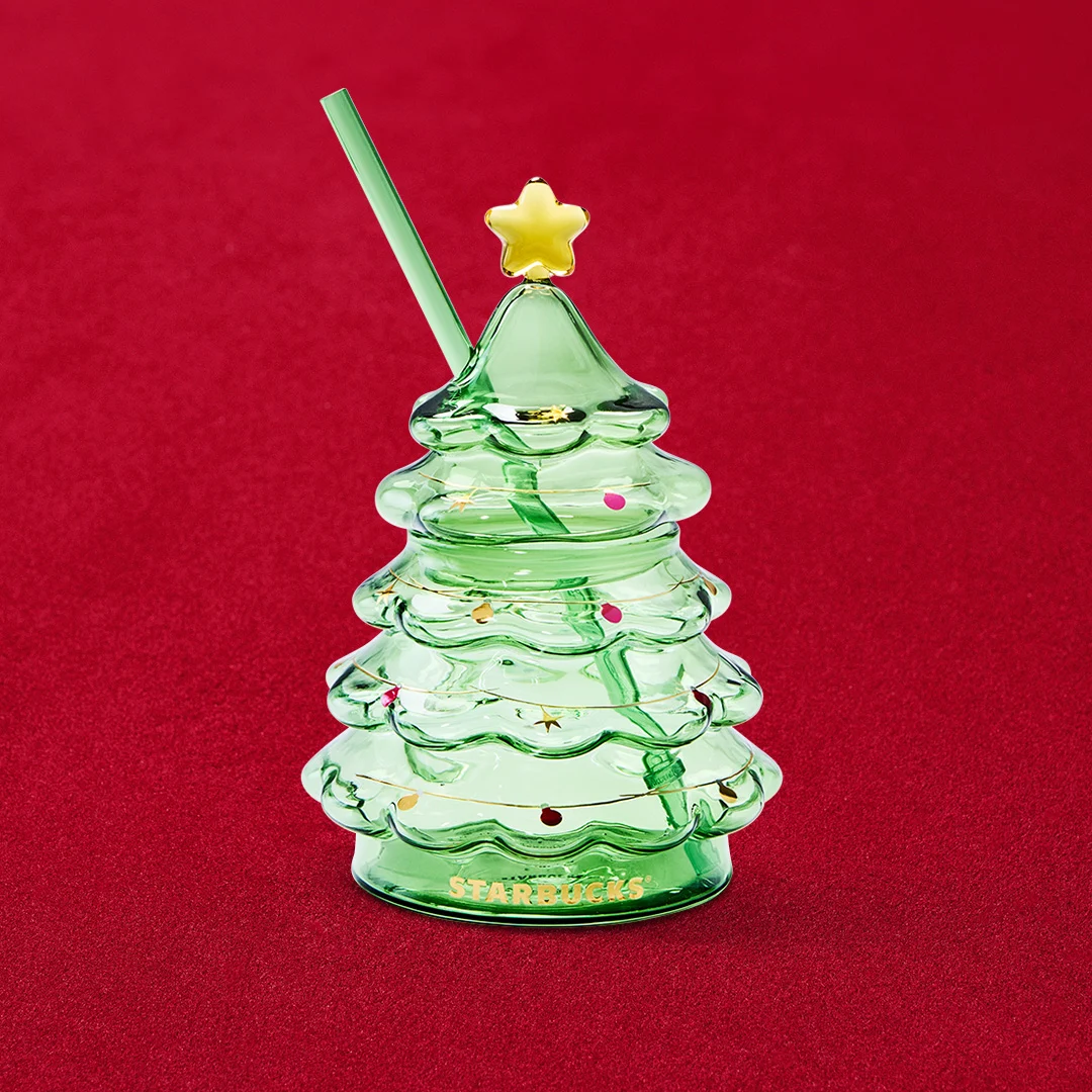A green glass cold cup shaped like a Christmas tree, with a gold star lid and a green straw