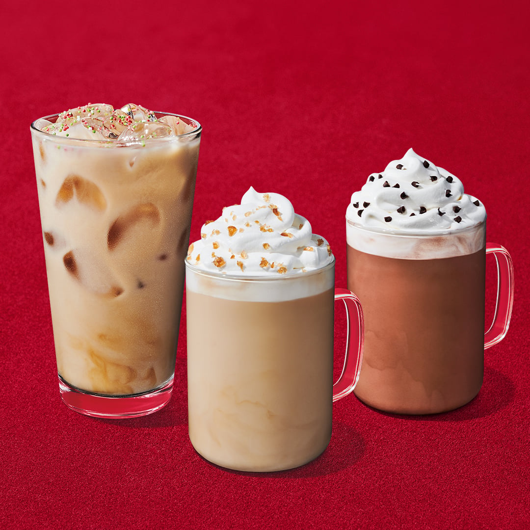 Three returning Starbucks holiday drinks on a red background, two topped with whipped cream