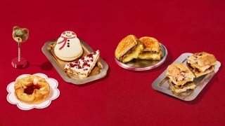 Starbucks' 2026 holiday food on a red tabletop: a bear-shaped cake pop, a snowman cookie, a cranberry bar, a cheese danish and two hot sandwiches