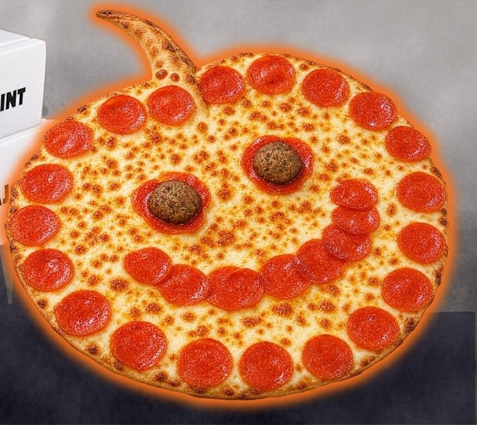 A pizza shaped like a jack-o'-lantern with a crust stem, a smile made of pepperoni slices, and two meatballs for eyes