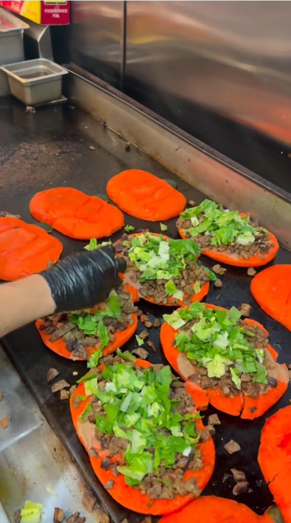 Orange pumpkin-shaped torta buns loaded with meat and lettuce on the flat-top grill at Tacotlán