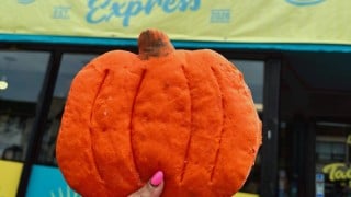 An orange pumpkin-shaped torta bun held up in front of the Tacotlán Express storefront in Chicago