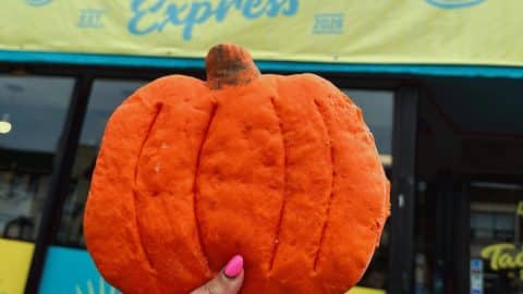 An orange pumpkin-shaped torta bun held up in front of the Tacotlán Express storefront in Chicago