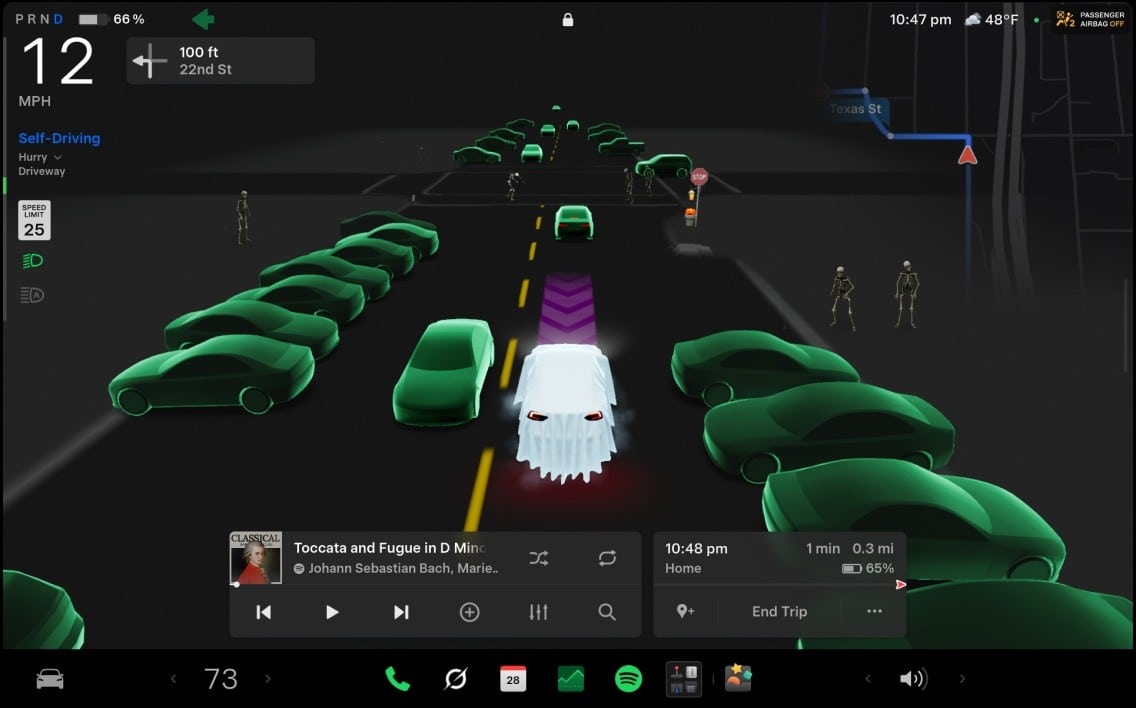 A car touchscreen shows a road where the driver's car is a white sheet ghost, the other cars are green and two skeletons stand on the sidewalk