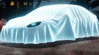 A car covered by a glowing white sheet with one eye hole showing sits in a foggy graveyard at night