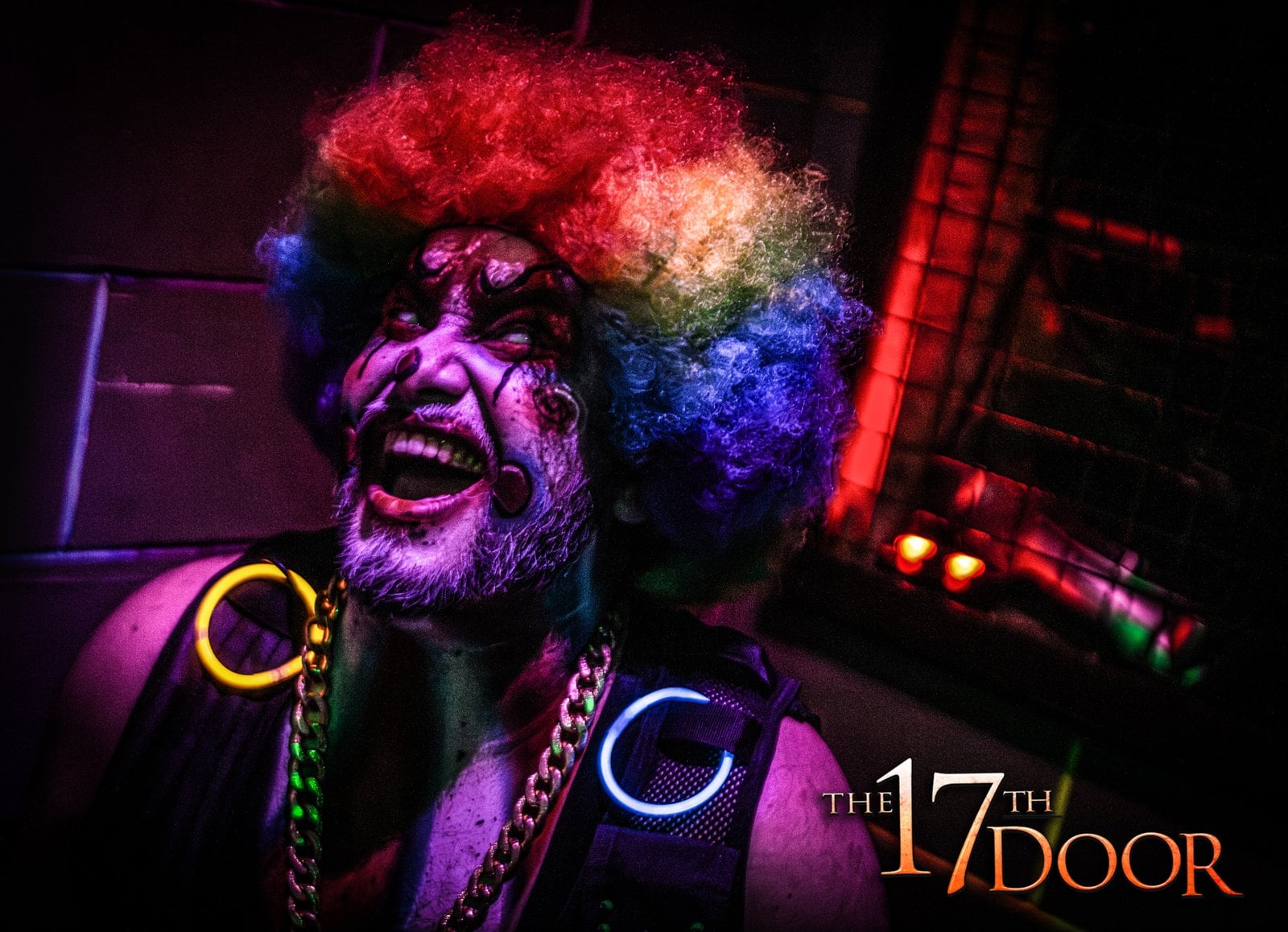A clown character in a rainbow wig laughs under purple light, wearing glow rings and a gold chain