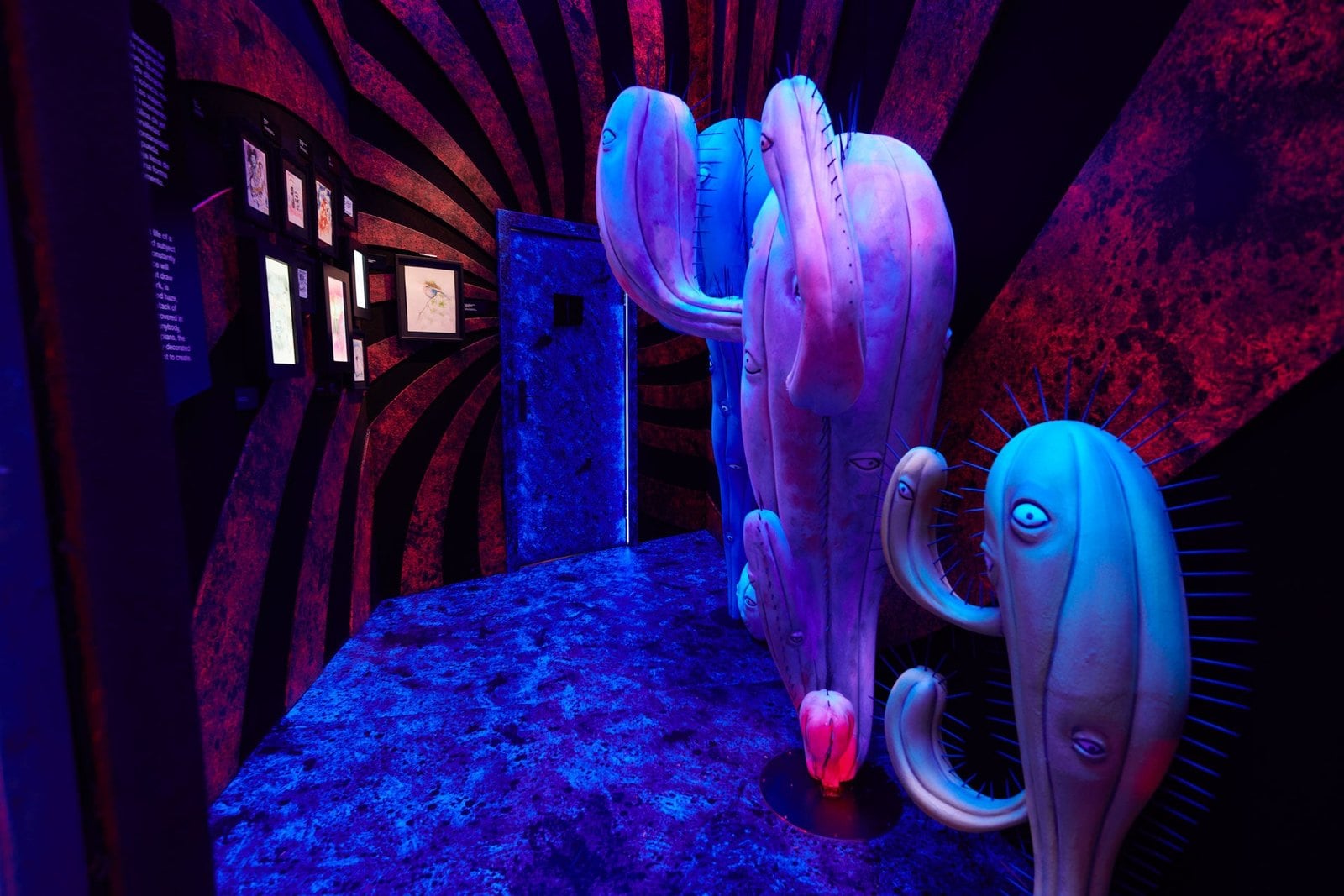 Blue creature sculptures in a room with a red-and-black spiral wall and framed drawings