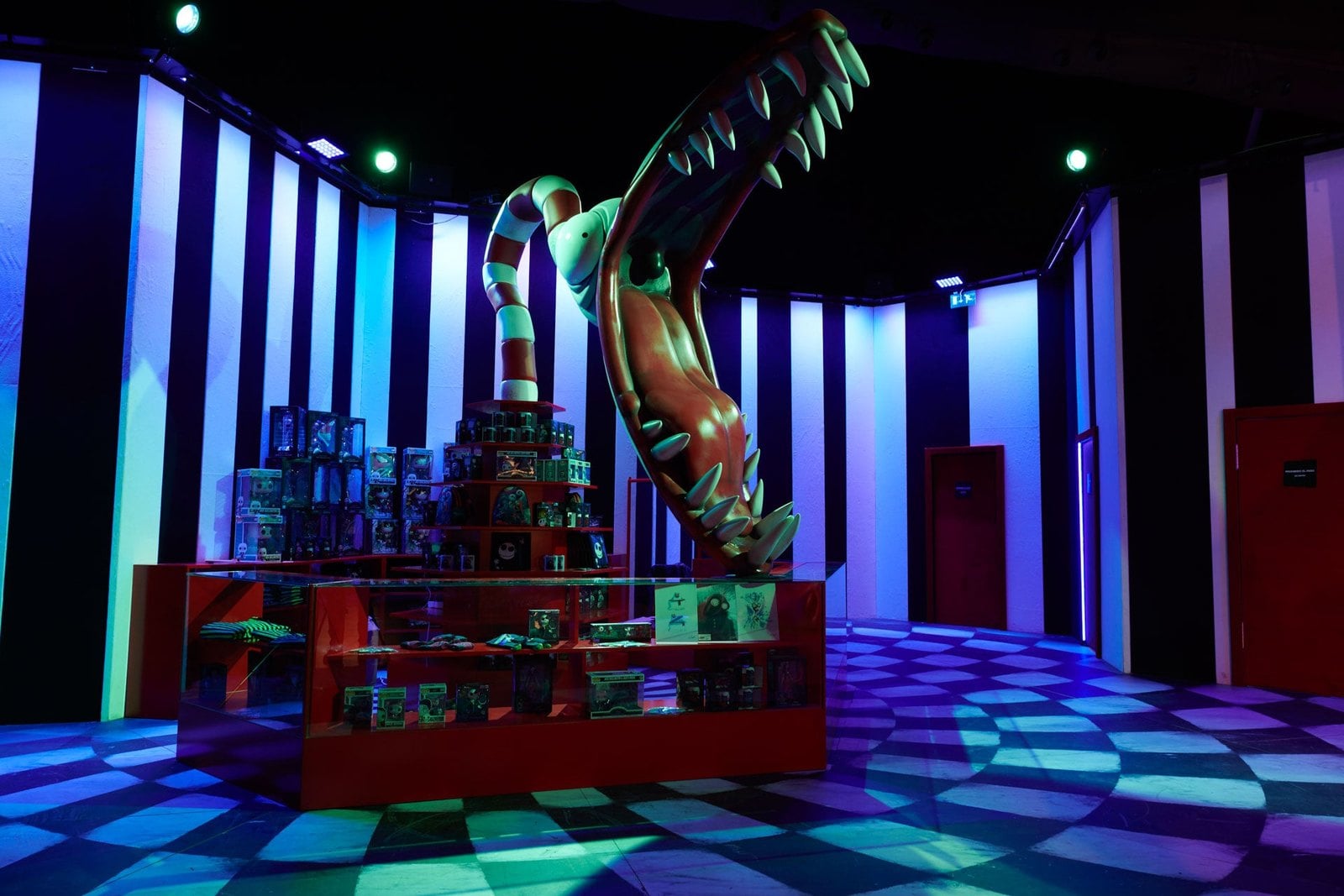 A giant black-and-white striped worm with open jaws rises over a glass counter of boxed merchandise in a blue-lit room