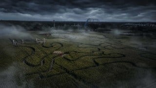 Toverland's Entwined corn maze at night under storm clouds and fog, with the winding maze paths and the Fenix coaster in the distance