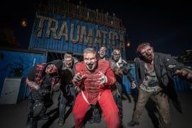Traumatica scare actors in zombie makeup posing in front of the Traumatica sign at Europa-Park at night