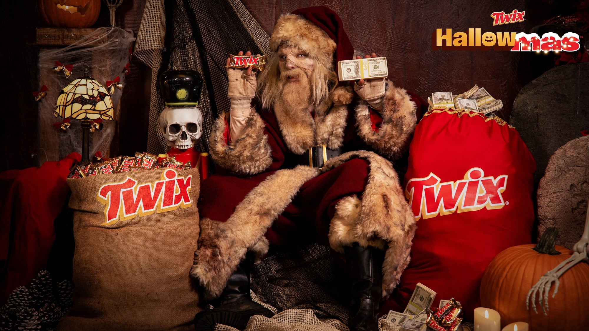 TWIX Hallowmas campaign image of Zombie Claus seated between a burlap sack of TWIX bars and a red sack of cash, with the Hallowmas logo in the corner