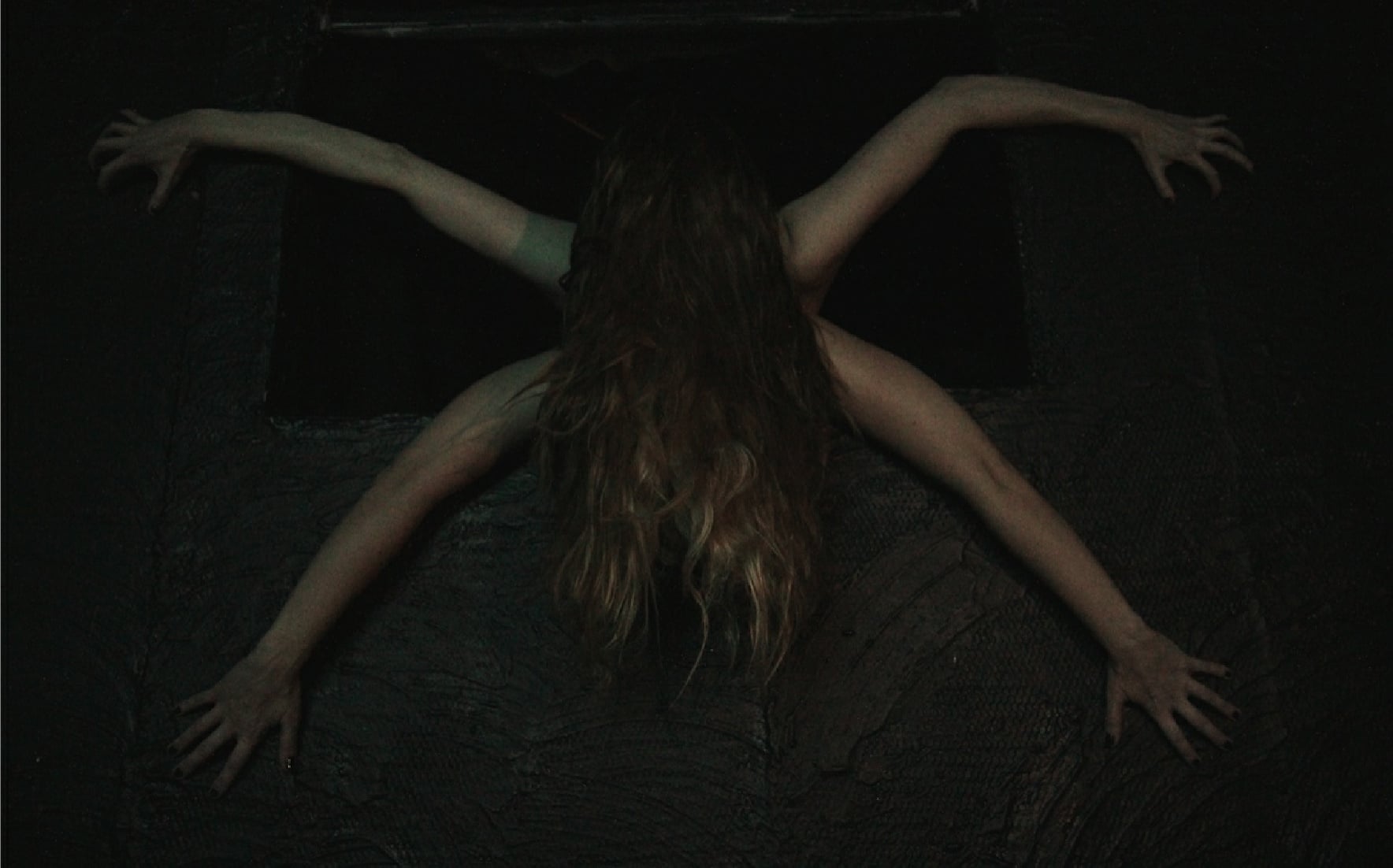 A long-haired performer emerges from darkness with arms outstretched during Urban Death at Zombie Joe's Underground Theatre.