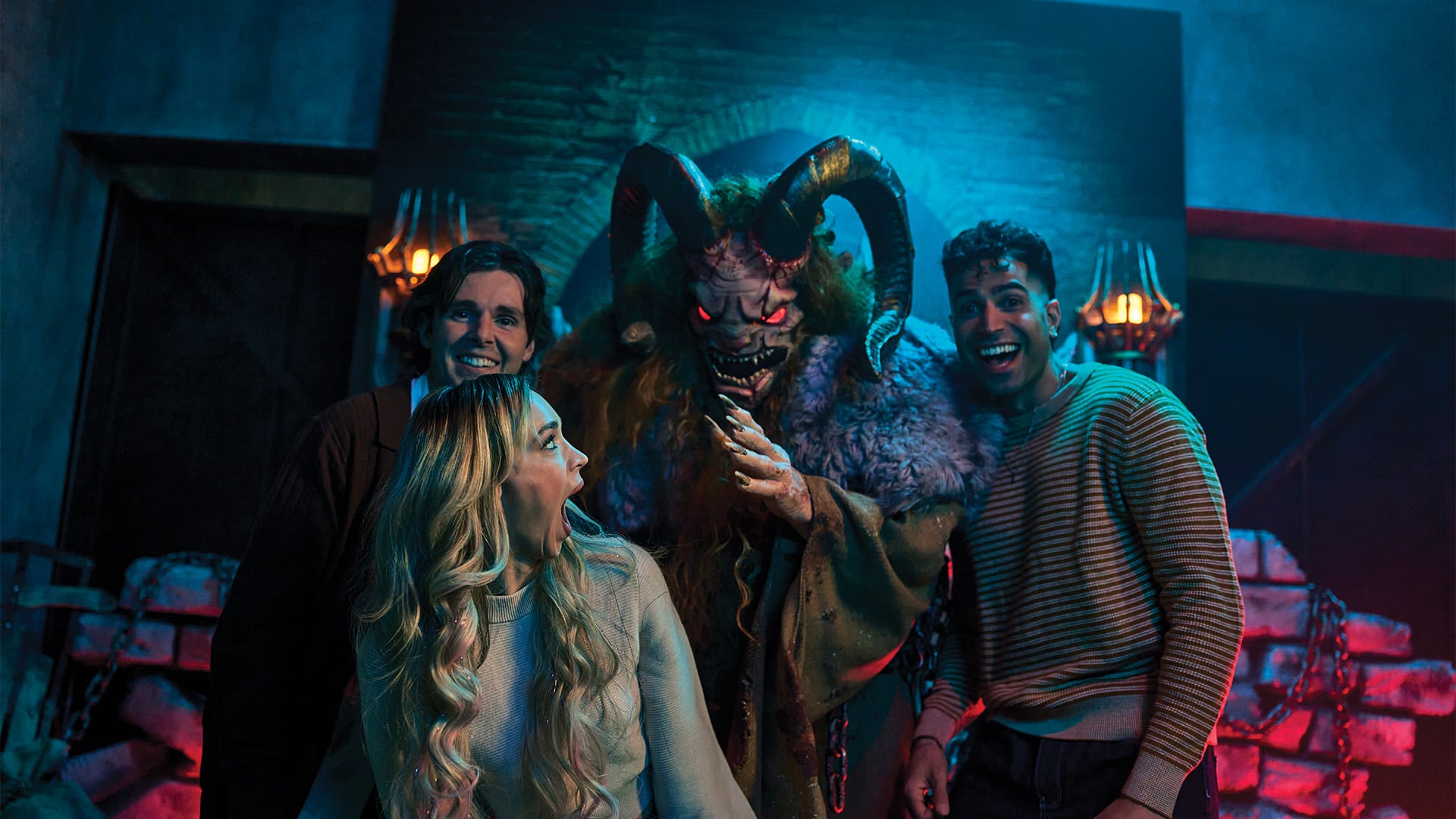 Three guests react as Krampus leans in behind them in front of a brick wall with lit sconces