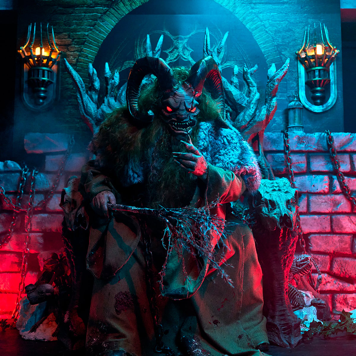 Krampus seated on a throne of skulls and twisted branches, holding a bundle of birch switches, in front of a brick wall hung with chains and lit sconces