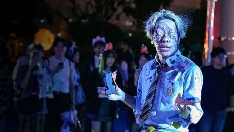A street zombie performer in a blood-spattered school uniform at Universal Studios Japan, with guests filming behind him