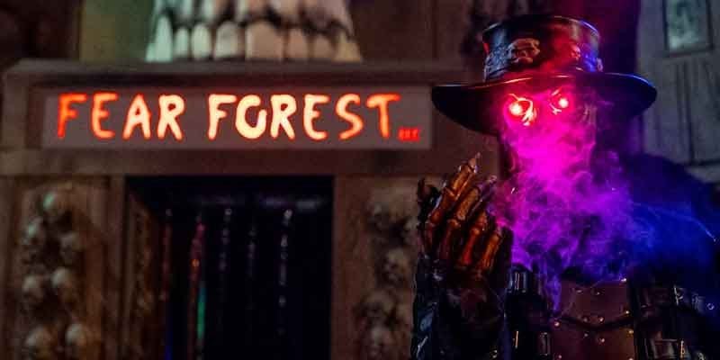 A figure in a top hat with glowing red eyes breathes purple smoke beside a lit Fear Forest sign