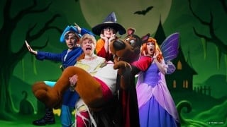 Scooby-Doo and the Mystery Inc. gang in Halloween costumes, a pirate, a mummy, a witch, a vampire and a fairy, in front of a haunted house