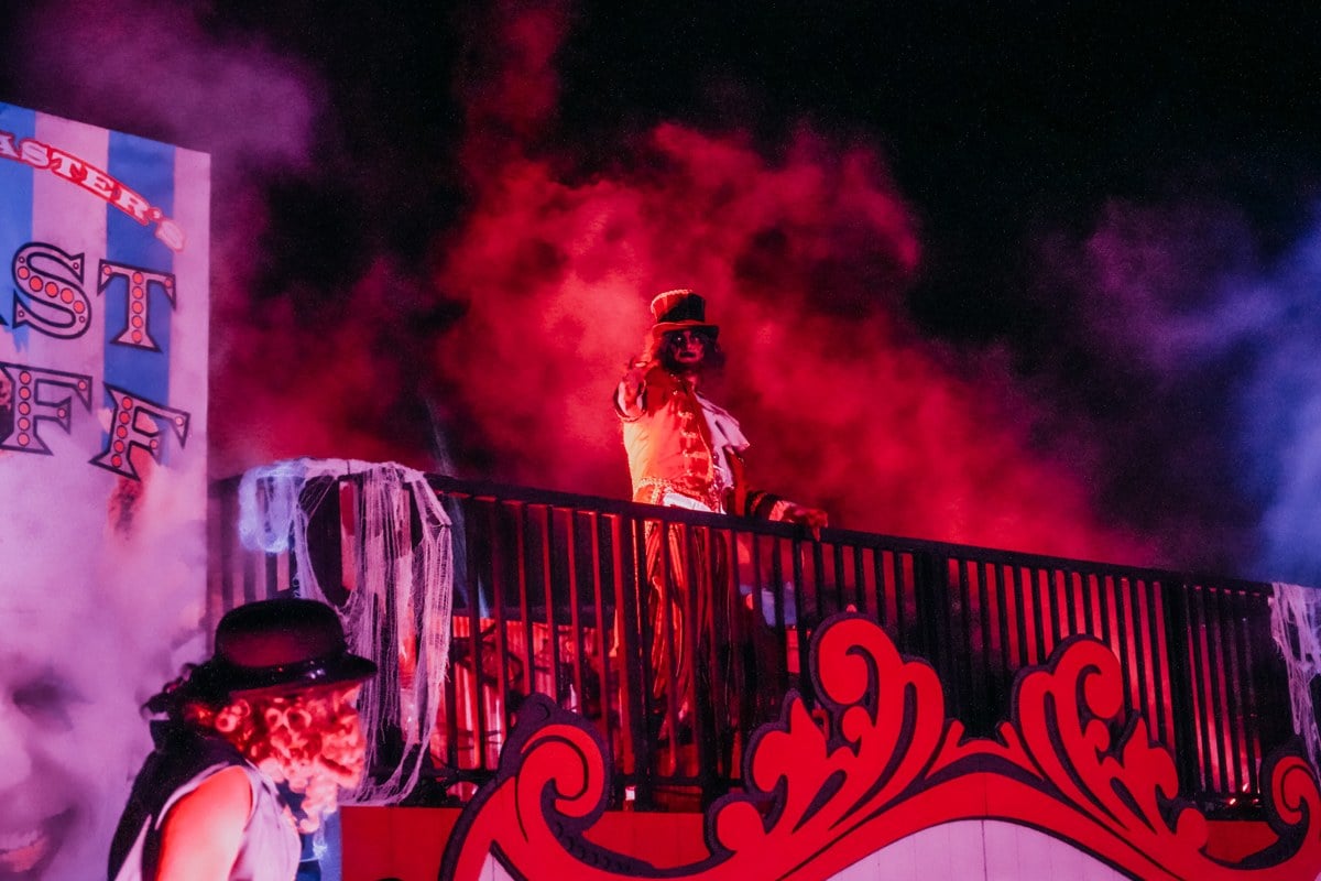 Performers in clown costumes on a red-lit stage filled with pink smoke