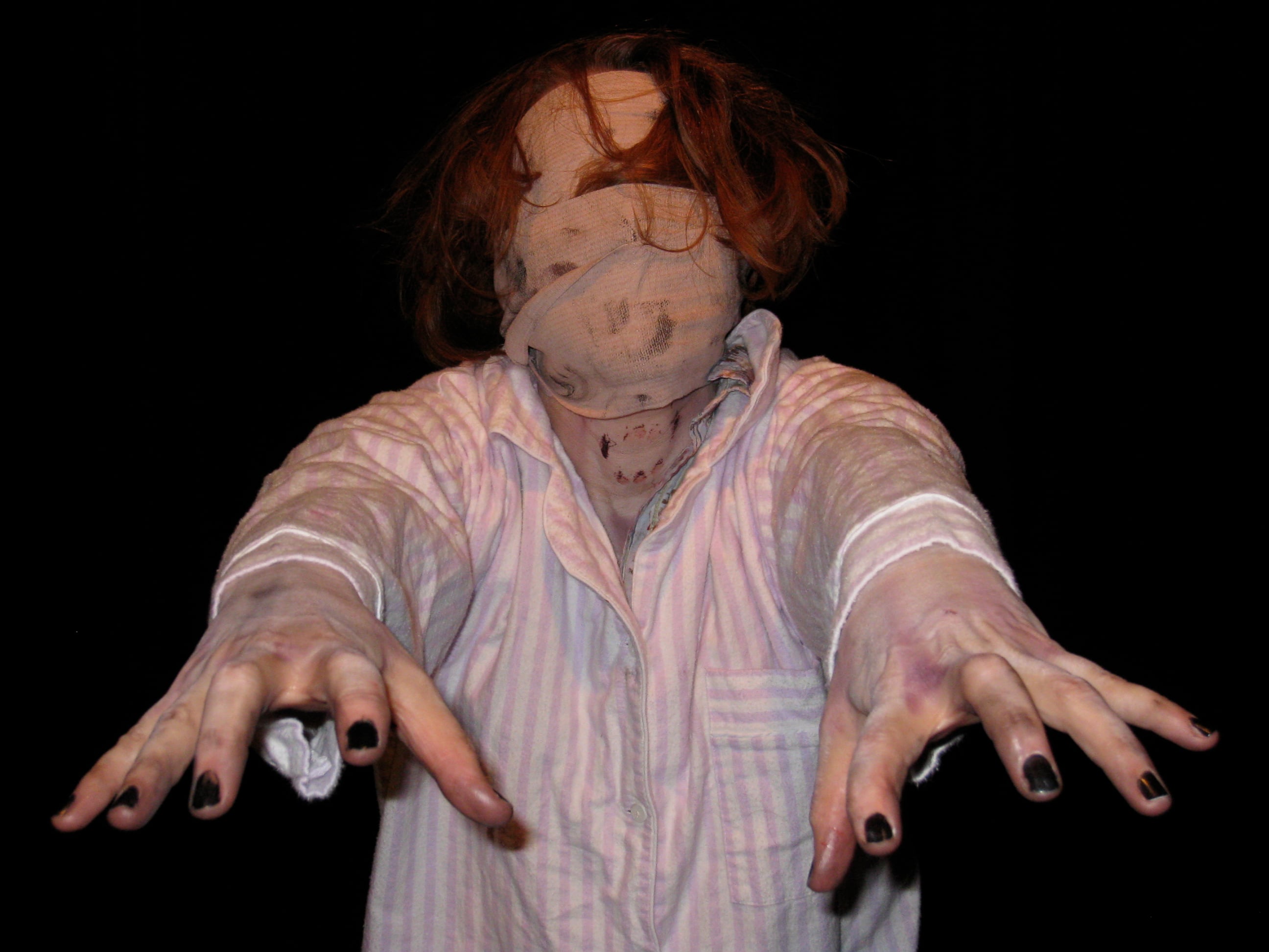 A performer in a striped nightshirt with a bandaged face reaches toward the camera during Urban Death.
